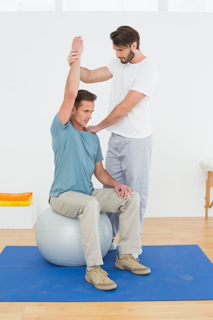 Mann auf dem Yogaball, der mit einem körperlichen Therapeuten arbeitet