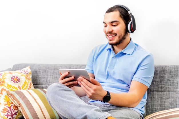 Mann auf Sofa mit Kopfhörern und digitalem Tablet