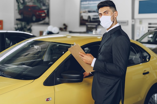 Mann Autohändler, der medizinische Schutzmaske an seinem Arbeitsplatz trägt