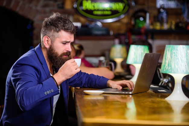 Mann bärtiger Geschäftsmann sitzen Kneipe mit Laptop und Tasse Kaffee. Freiberuflicher Benefit Manager arbeiten online, während Sie Kaffee genießen