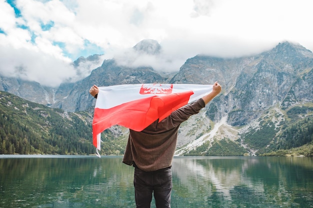 Mann bedeckt mit polnischer Flagge, die am Rand steht und auf den See in den Bergen blickt