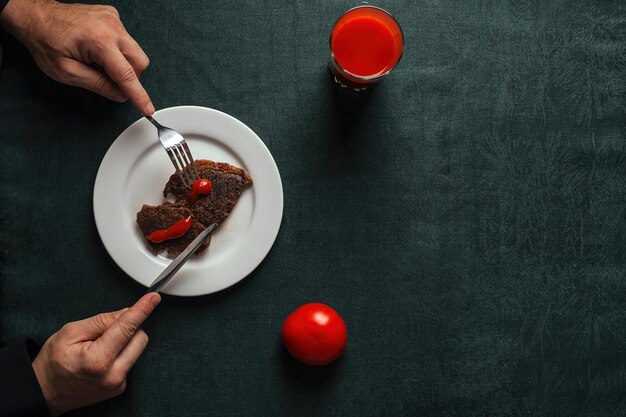 Mann beim Abendessen bestehend aus köstlichem gegrilltem Rindersteak und hellrotem Tomatensaft Draufsicht