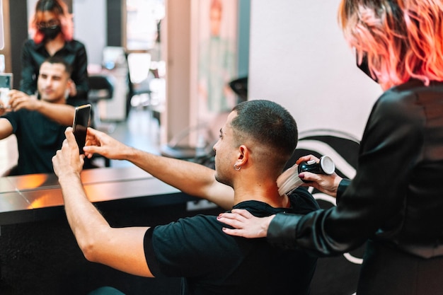 Mann beim Friseur macht ein Selfie mit einem Smartphone, nachdem er sich die Haare geschnitten hat