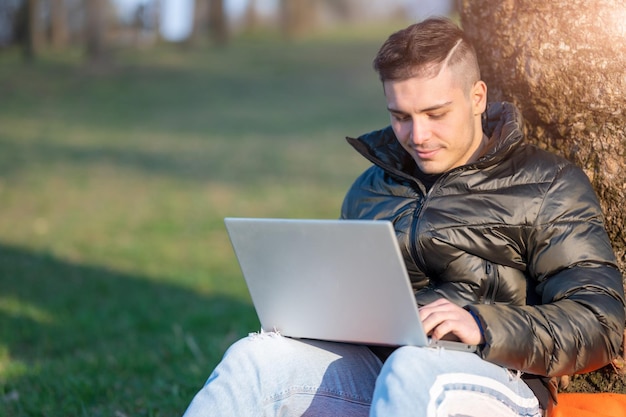 Mann benutzt Laptop, während er auf dem Feld sitzt