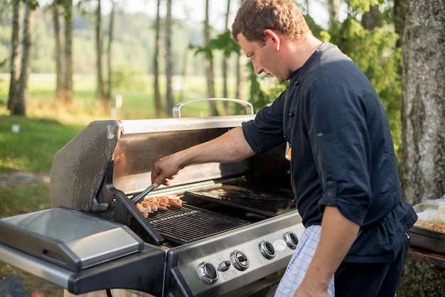 Mann bereitet Essen auf dem Grill gegen Bäume vor