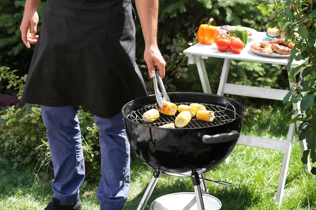 Mann bereitet köstlichen Mais auf dem Grill im Freien zu