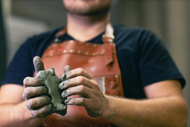 Foto mann bildhauer gekleidet lederschürze mit ton in händen statue craft creation workshop