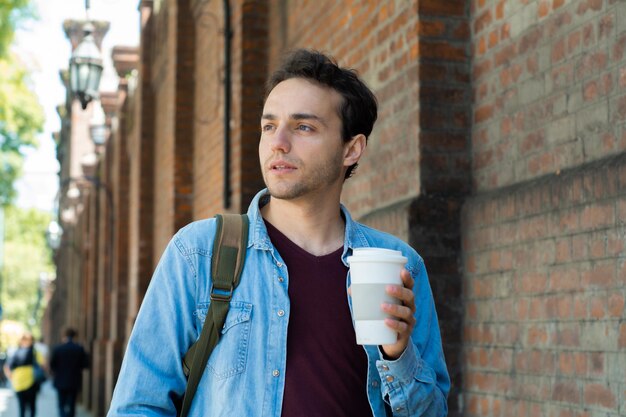 Foto mann blickt weg, während er eine kaffeetasse an der wand hält