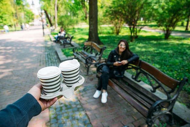 Mann bringt Kaffee für junge Frau im Stadtpark