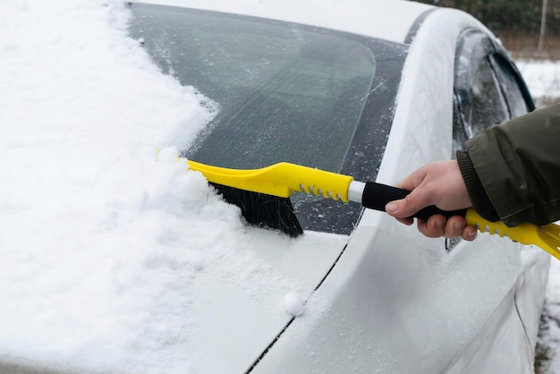 Mann bürstet Schnee von der Windschutzscheibe des Autos und reinigt Neuschnee nach SchneesturmSchneeschicht Windschutzscheibe