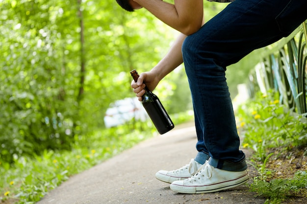 Mann deprimiert mit Bierflasche, die auf grünem Zaun im Freien sitzt. Menschen Alkoholismus-Probleme.