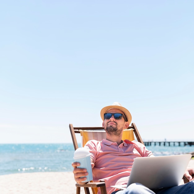 Foto mann, der am laptop am strand arbeitet, während getränk genießt