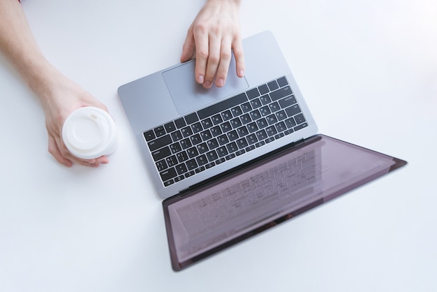 Mann, der an einem Laptop arbeitet und eine Tasse Kaffee auf einem weißen Hintergrund hält