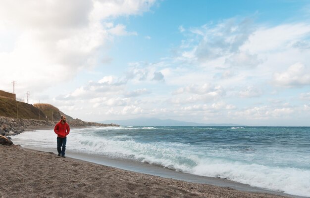 Mann, der an einem schönen bewölkten Tag an einem Strand mit aufgewühltem Wasser spazieren geht