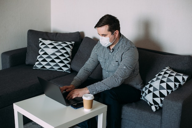 Mann, der an Laptop arbeitet, der Maske vom Hauptbüro trägt