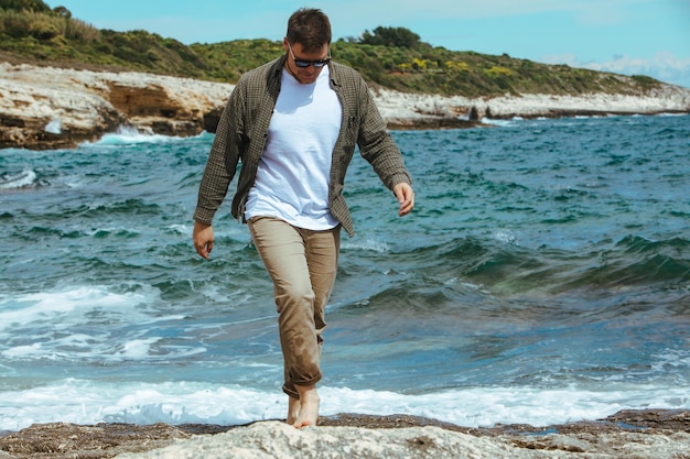 Mann, der an windigen Sommerferien am felsigen Strand spazieren geht, genießt die Sommerzeit mit Meerblick