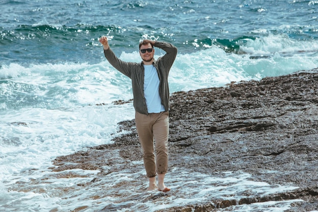 Mann, der an windigen Sommerferien am felsigen Strand spazieren geht, genießt Meerblick