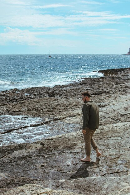 Mann, der an windigen Sommerferien am felsigen Strand spazieren geht, genießt Meerblick