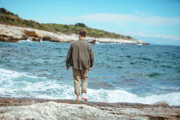 Mann, der an windigen Sommerferien am felsigen Strand spazieren geht, genießt Meerblick
