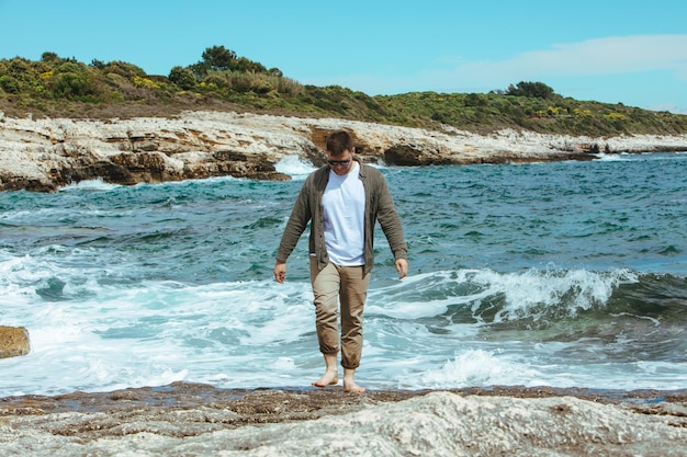 Mann, der an windigen Sommerferien am felsigen Strand spazieren geht, genießt Meerblick