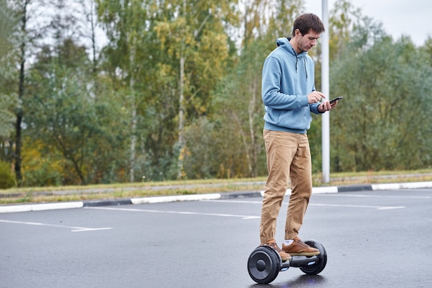 Mann, der auf das Hoverboard reitet und den Smartphone im Freien verwendet