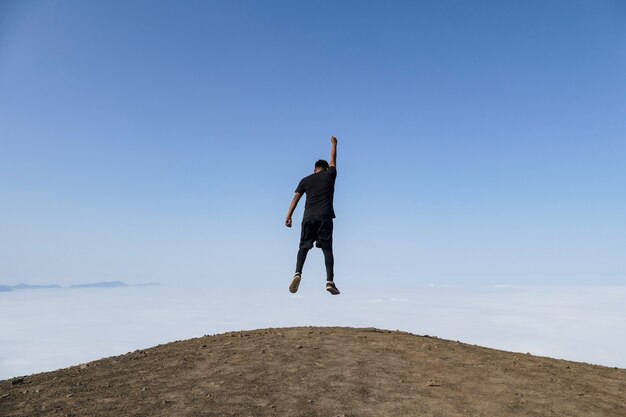 Mann, der auf einem Hügelhintergrund des blauen Himmels und der Wolken abhebt