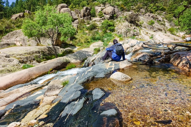 Mann, der auf einigen Felsen sitzt und von Wasserströmen und Wasserfällen umgeben ist