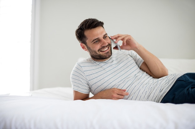 Mann, der auf Handy im Schlafzimmer zu Hause spricht