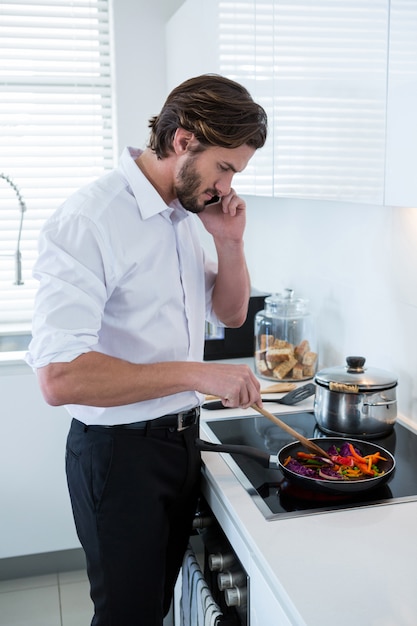 Mann, der auf Handy spricht, während Essen in der Küche vorbereitet