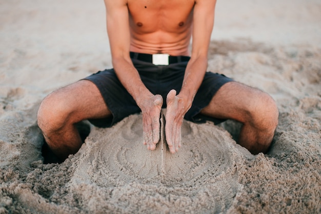 Mann, der auf Sand sitzt und Sandfiguren schafft.