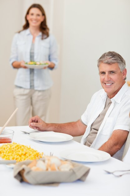 Mann, der auf seine Frau wartet, um Salat zum Tisch zu holen