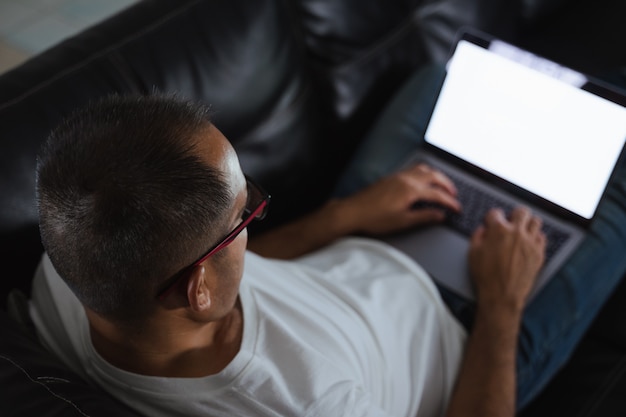 Mann, der auf Sofa sitzt und Computer-Laptop für Arbeit oder Entspannung zu Hause verwendet. Arbeit von zu Hause aus Konzept.