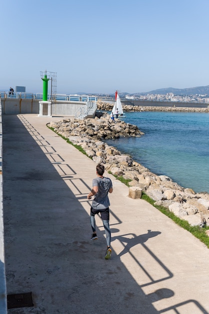 Mann, der bei klarem Himmel in Richtung Hafenleuchtturm rennt, trägt Sportkleidung