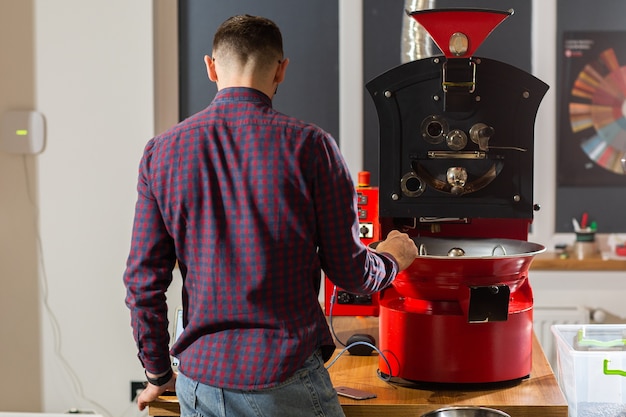 Mann, der bei romatischen Kaffeebohnen beobachtet, die sich in moderner Ausrüstung mit Getreidekühler befinden. Branchenkonzept. moderne Maschine zum Rösten von Bohnen. Kaffeeröster wird in den Kühlzylinder gegossen.