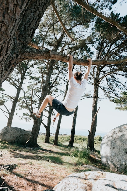 Foto mann, der beim spielen an einem baum hängt, freiheits- und freiheitskonzept, weißes t-shirt, waldstrand