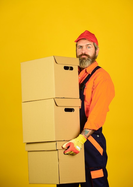Foto mann, der boilersuit-verpackungsboxen trägt, zieht in eine neue wohnung um bärtiger lader in uniform kartons, die in ein neues haus ziehen, kauf einer neuen wohnung oder reparatur von räumen