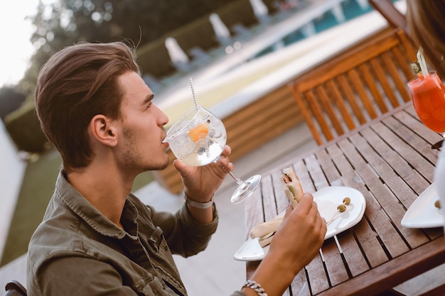 Mann, der Cocktail trinkt und in der Nähe des Pools zu Mittag isst