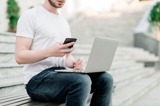 Mann, der das Telefon und Laptop im Freien verwendet