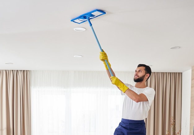 Mann, der Decke und Lampen im Wohnzimmer reinigt. Hausreinigungsservice-Konzept.