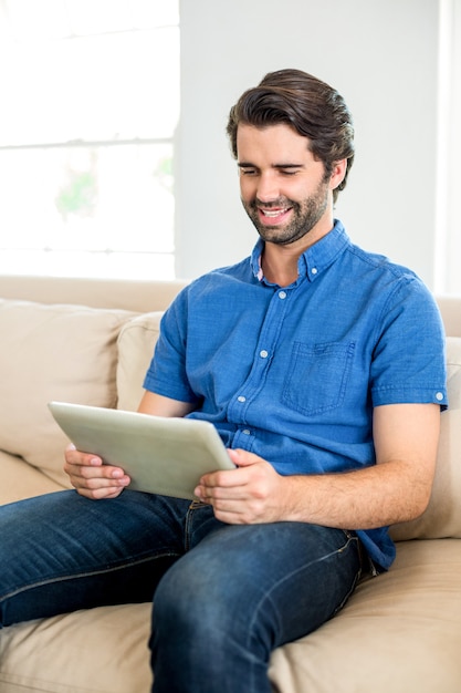 Mann, der digitale Tablette beim auf Sofa zu Hause sitzen verwendet