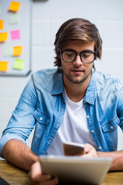 Mann, der digitales Tablett und Handy im Büro verwendet