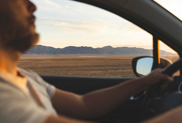 Mann, der ein Auto fährt Schöne Natur und Berge bei Sonnenuntergang im Seitenfenster