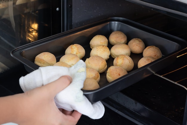 Mann, der ein Backblech mit Käsebrötchen aus einem Elektroofen oder Pao de Queijo auf Portugiesisch nimmt