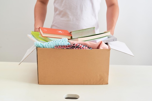 Foto mann, der ein buch und kleidung hält, spendet kasten. spendenkonzept.