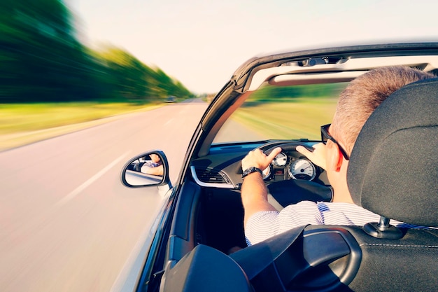 Mann, der ein Cabrio auf der Landstraße fährt Blick von innen hinter dem Fahrer Mann fährt mit hoher Geschwindigkeit auf der Autobahn Gefährliches schnelles Fahren Bewegungsunschärfe-Effekt