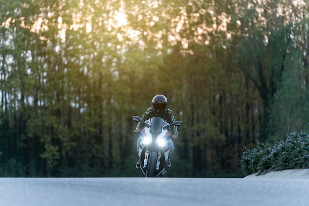 Mann, der ein großes Motorrad auf einer leeren Straße mit eingeschalteten Lichtern fährt