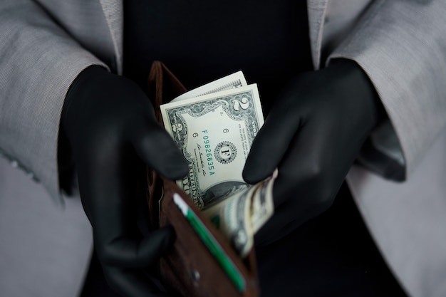 Mann, der eine Brieftasche mit Gelddollar in der Hand mit schwarzen medizinischen Handschuhen hält.