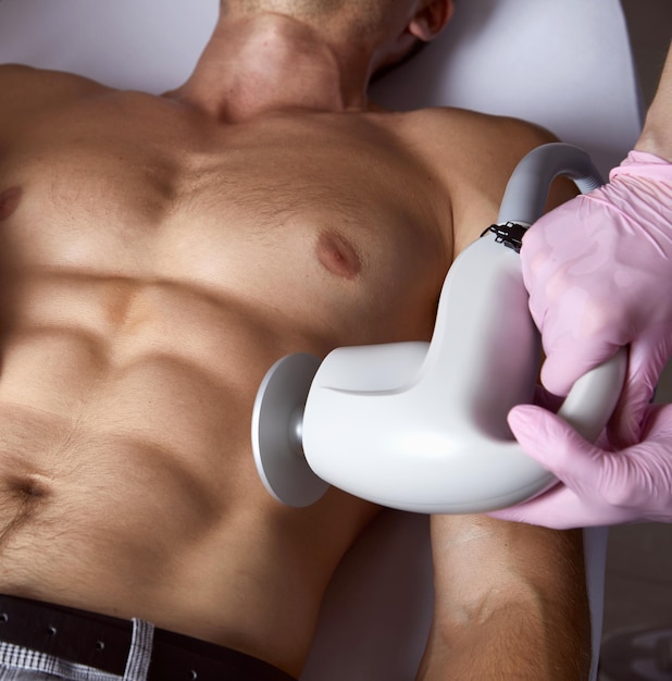 Mann, der eine fettreduzierende Hautlifting-Körperbehandlung auf modernen Geräten in einer Kosmetikklinik erhält
