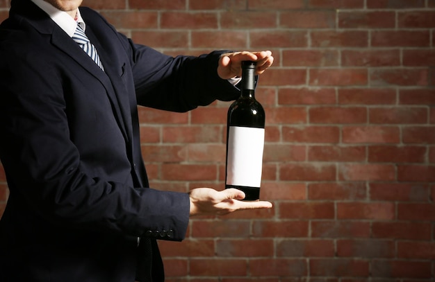 Mann, der eine Flasche Rotwein in den Händen auf Backsteinmauerhintergrund hält