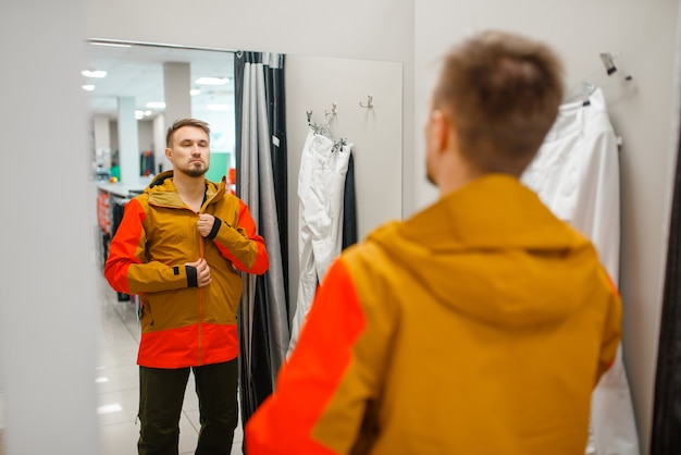 Mann, der eine Jacke für Ski oder Snowboarden, Sportgeschäft anprobiert.